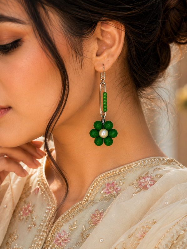 Woman wearing green safety pin earrings with floral pearl design and modern western outfit closeup