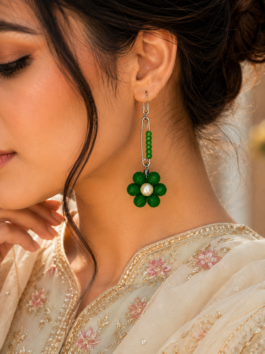 Woman wearing green safety pin earrings with floral pearl design and modern western outfit closeup